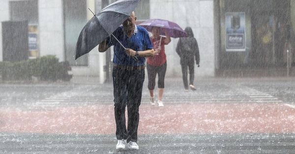 Foto: Varias personas cruzan una calle tratando de protegerse con un paraguas de una fuerte tormenta en Valencia. (EFE)