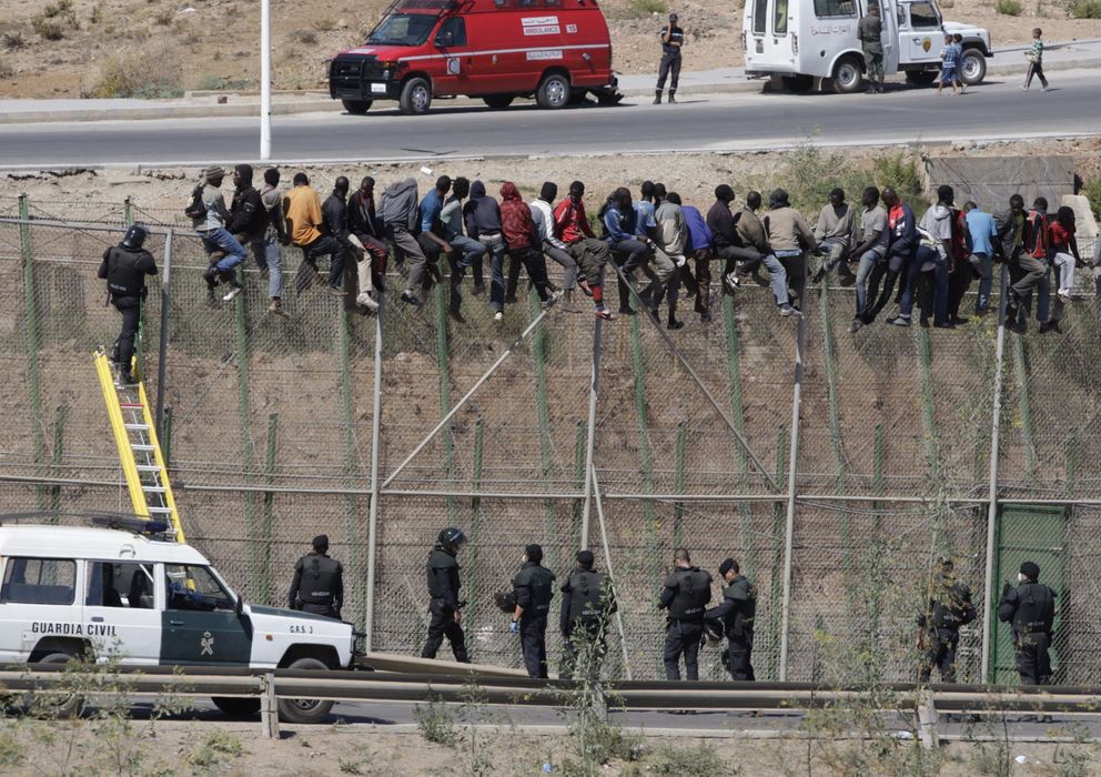 Foto: Dos de los inmigrantes bajan de la valla tras horas encaramados a ella (Efe)