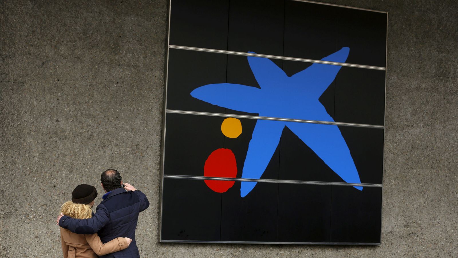 Foto: Una pareja se toma una foto frente al logo del Caixabank. (Reuters)
