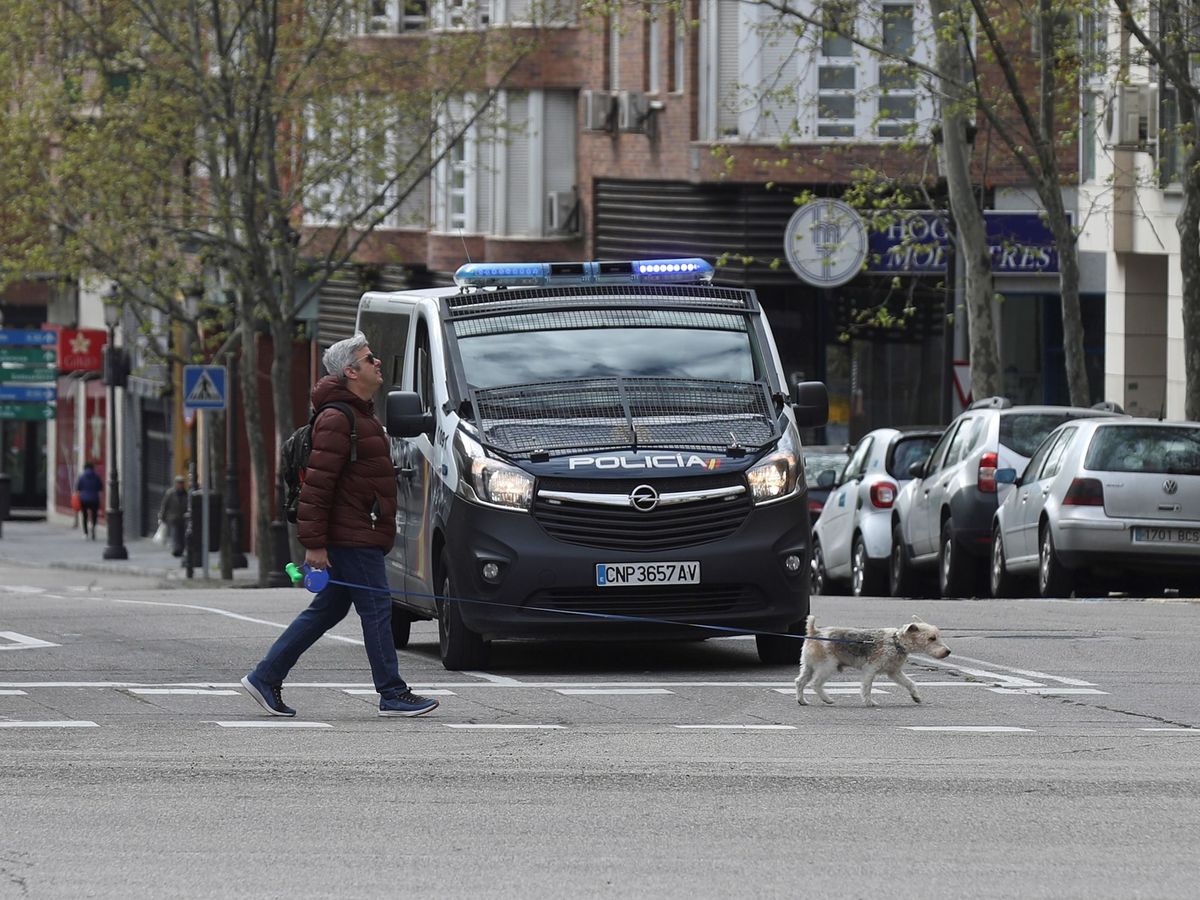 Foto: Un hombre pasea a su perro ante un furgón de la Policía Nacional durante el estado de alarma. (EFE)