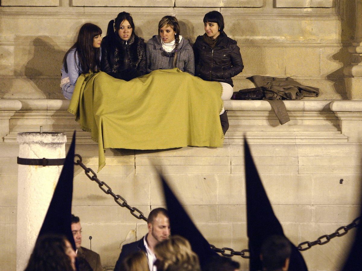 Foto: Varias jóvenes se protegen del frío con una manta en una noche de la Semana Santa en Sevilla. (EFE/Eduardo Abad)