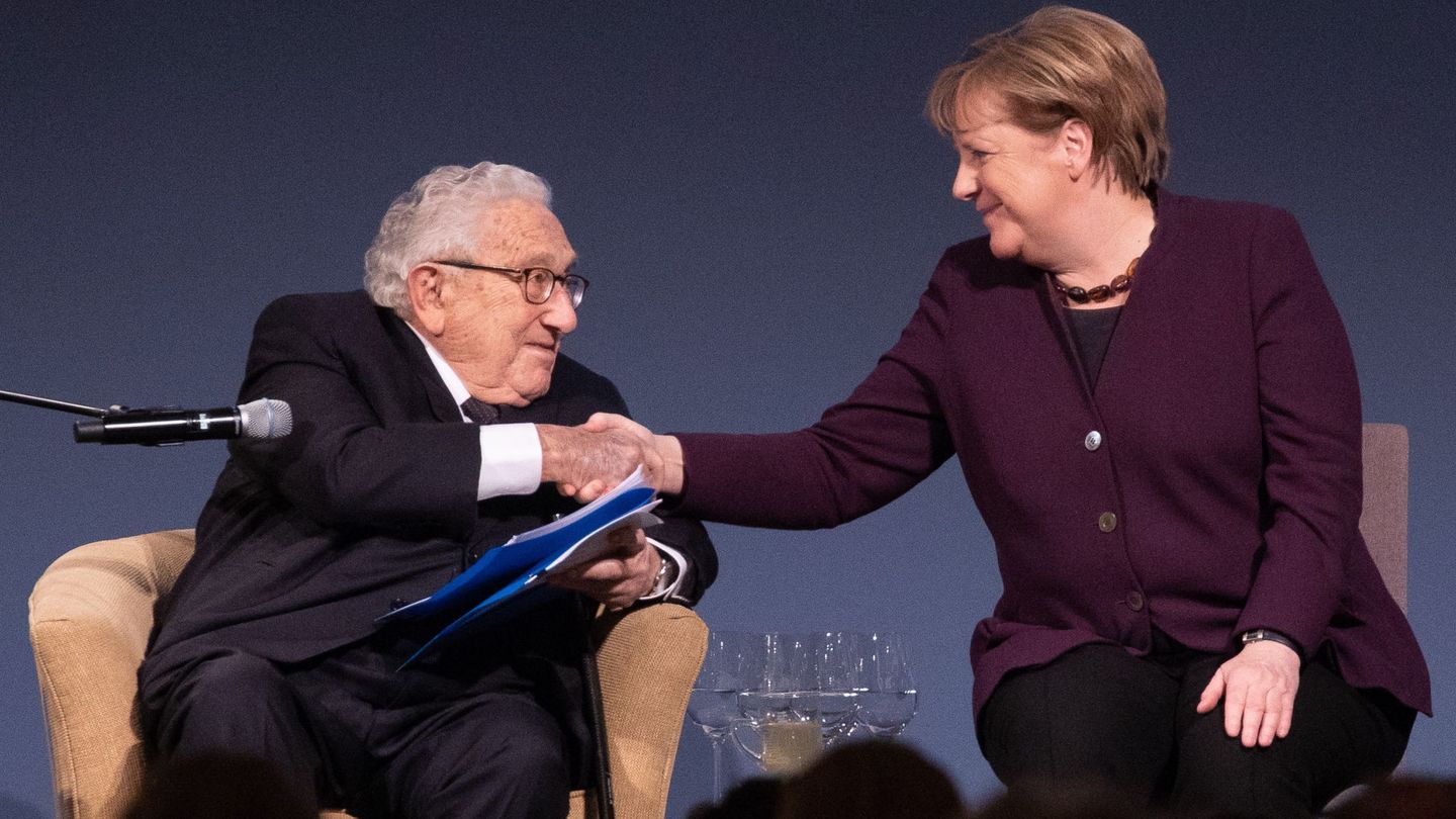 Henry Kissinger estrecha la mano de Angela Merkel. (EFE)