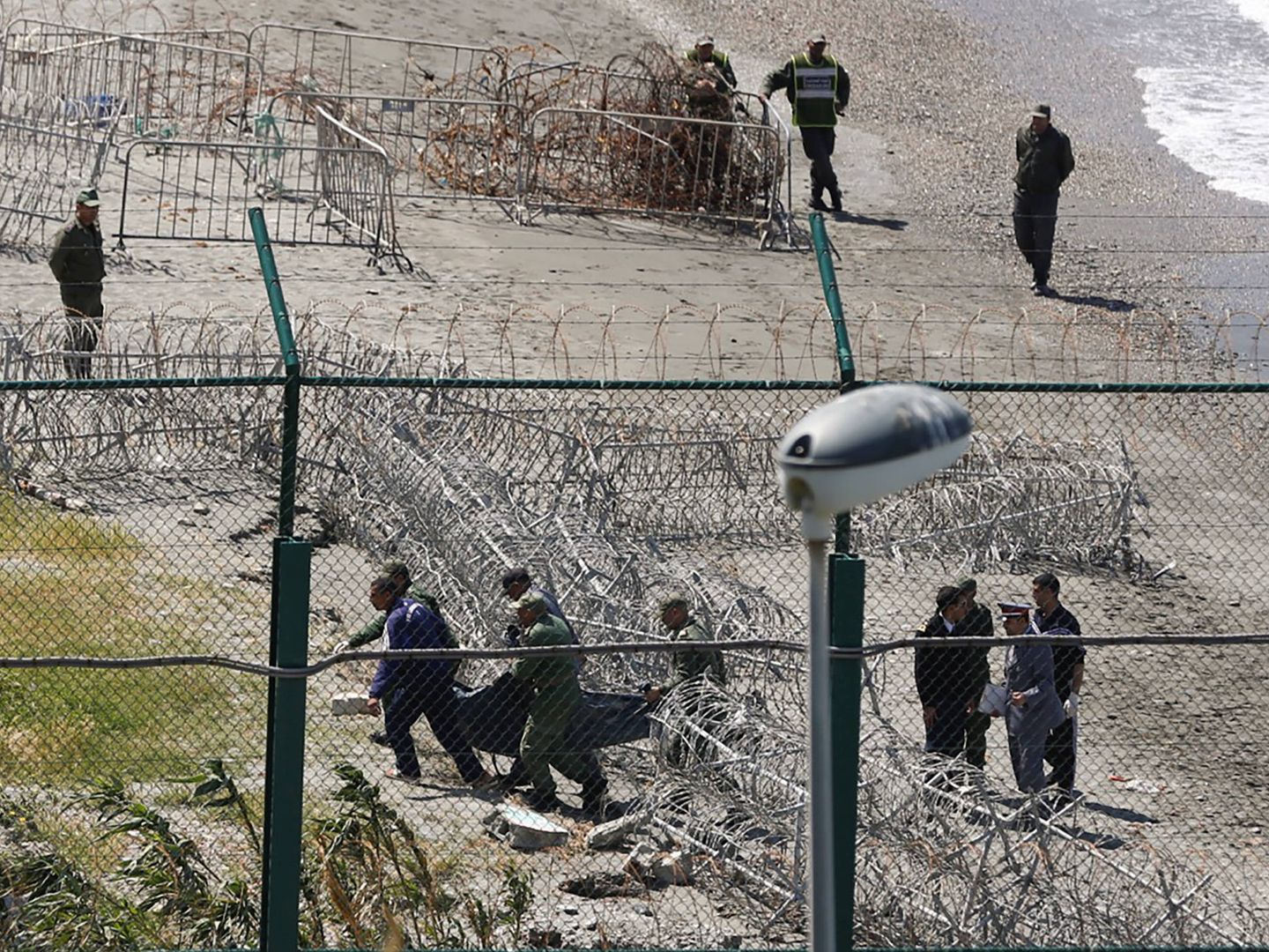 Agentes marroquíes trasladan el cadáver de un migrante que intentó cruzar a España en la playa de Belyounech. (Reuters) 