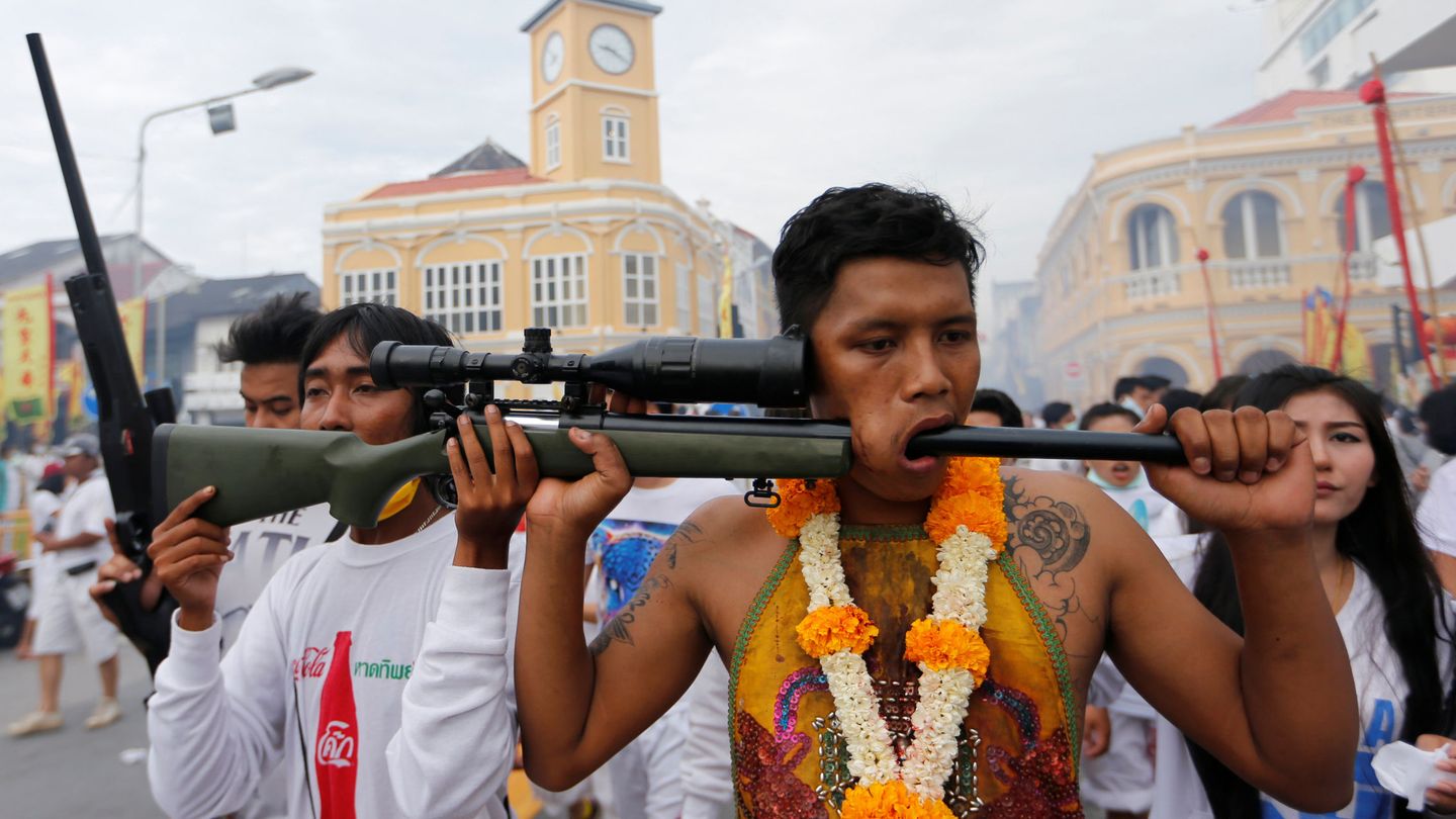 Un deboto de un santuario utiliza un arma para mostrar su mejilla perforada durante un festival en Tailandia. (Reuters)