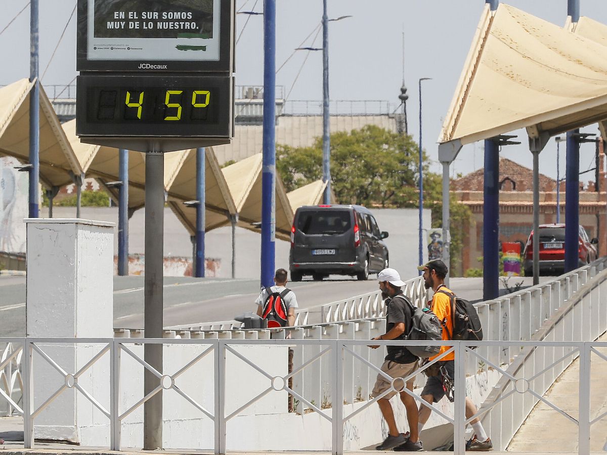 Foto: Dos hombres pasan por delante de uno de los termómetros que marcan la temperatura en Sevilla. (EFE / José Manuel Vidal)