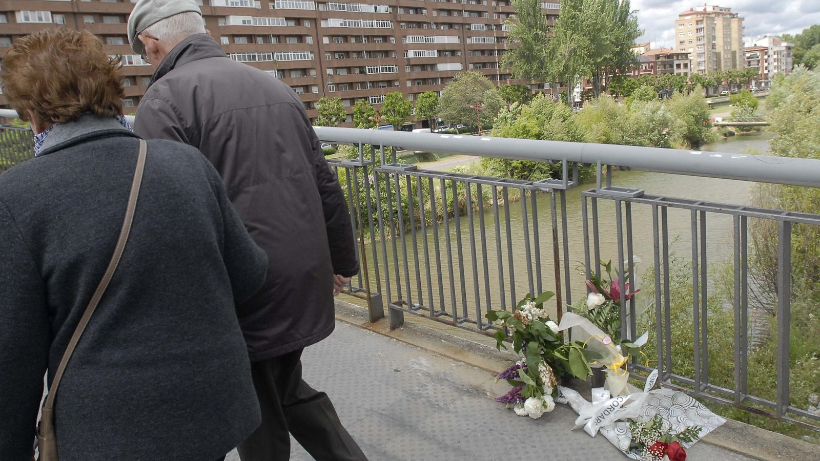 Foto: Dos personas pasan junto a flores depositadas en la pasarela en la que fue asesinada la presidenta de la Diputación de León, Isabel Carrasco. (EFE) 