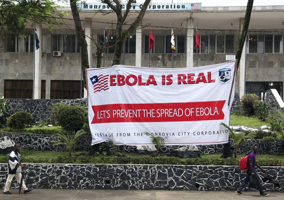 Foto: Varios liberianos caminan frente a un cartel que alerta sobre los peligros del ébola en el Ayuntamiento de Monrovia. (EFE)
