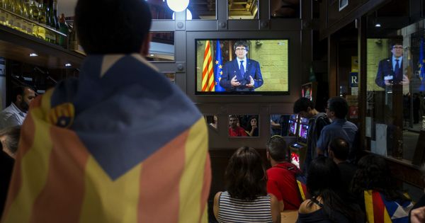 Foto: Un grupo de ciudadanos sigue desde una pantalla de televisión la declaración institucional del presidente de la Generalitat. (EFE)