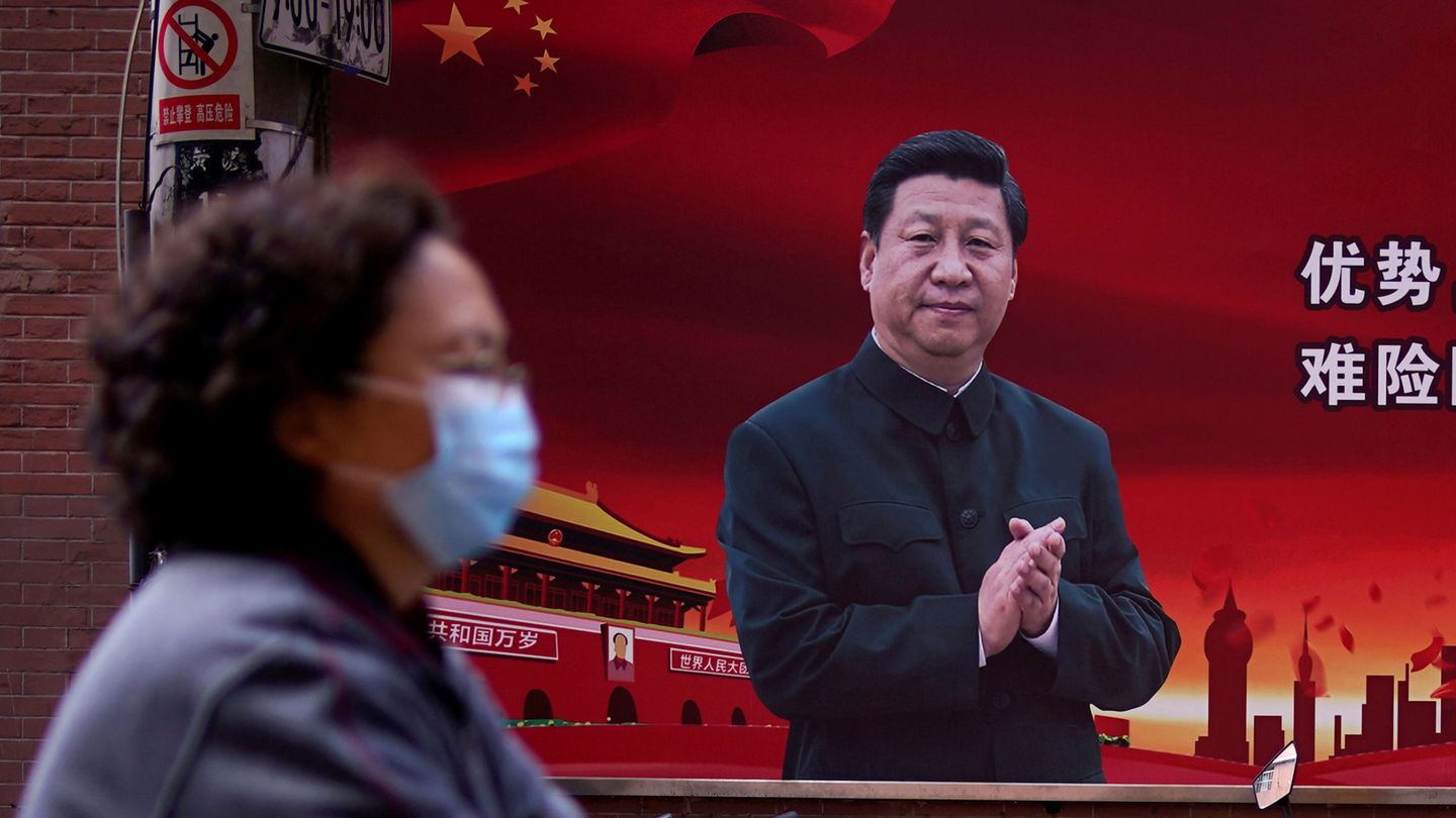 Una mujer con mascarilla pasa por delante de un mural con la imagen de Xi Jinping. (Reuters)