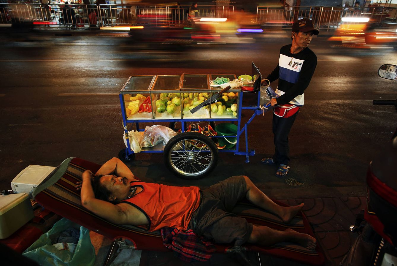 Foto: A street vendor pulls his cart by a sleeping man as cars pass by in Bangkok's Chinatown