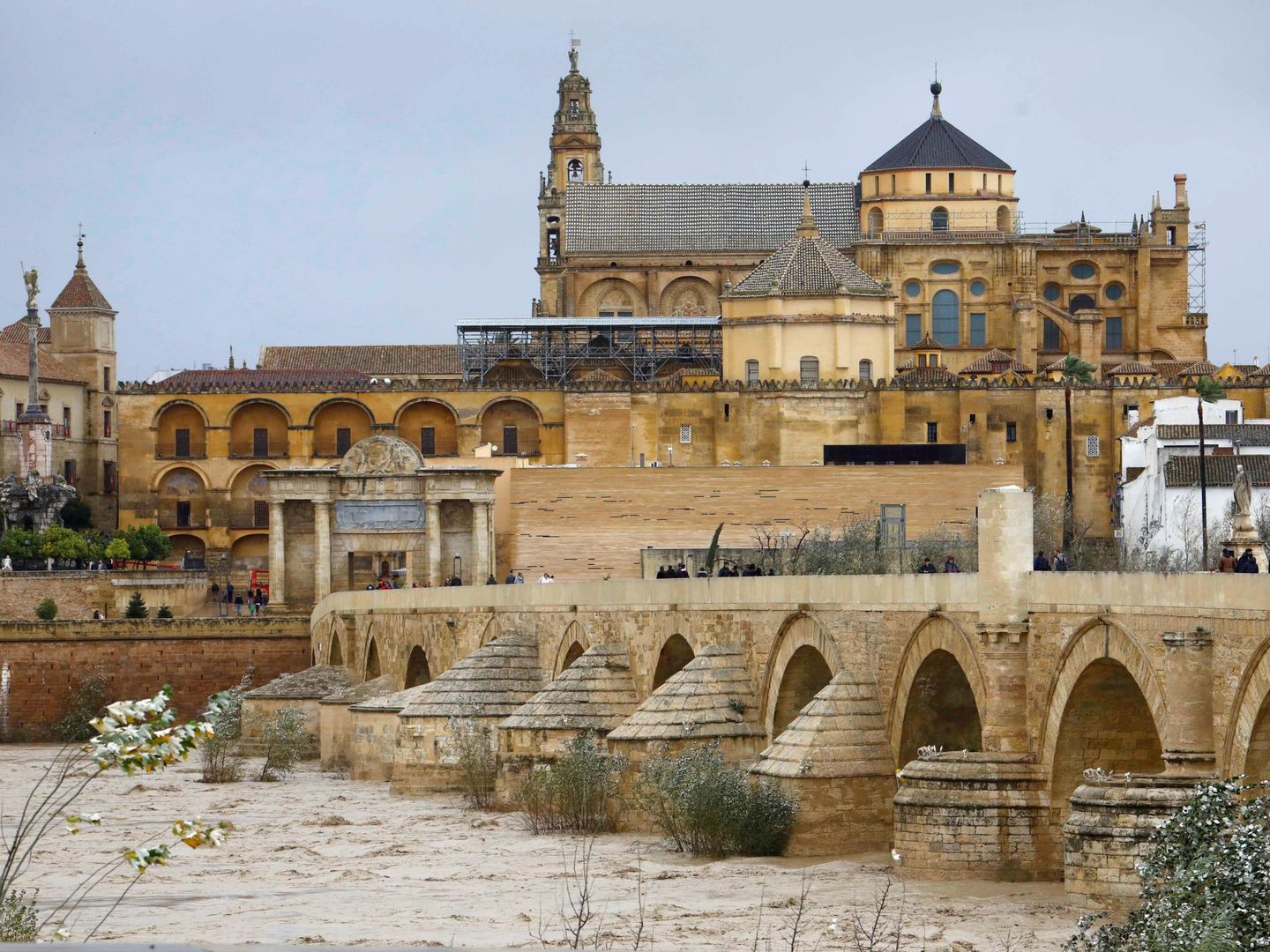 Varios transeúntes observan la crecida del río Guadalquivir por el puente romano de Córdoba. (EFE)