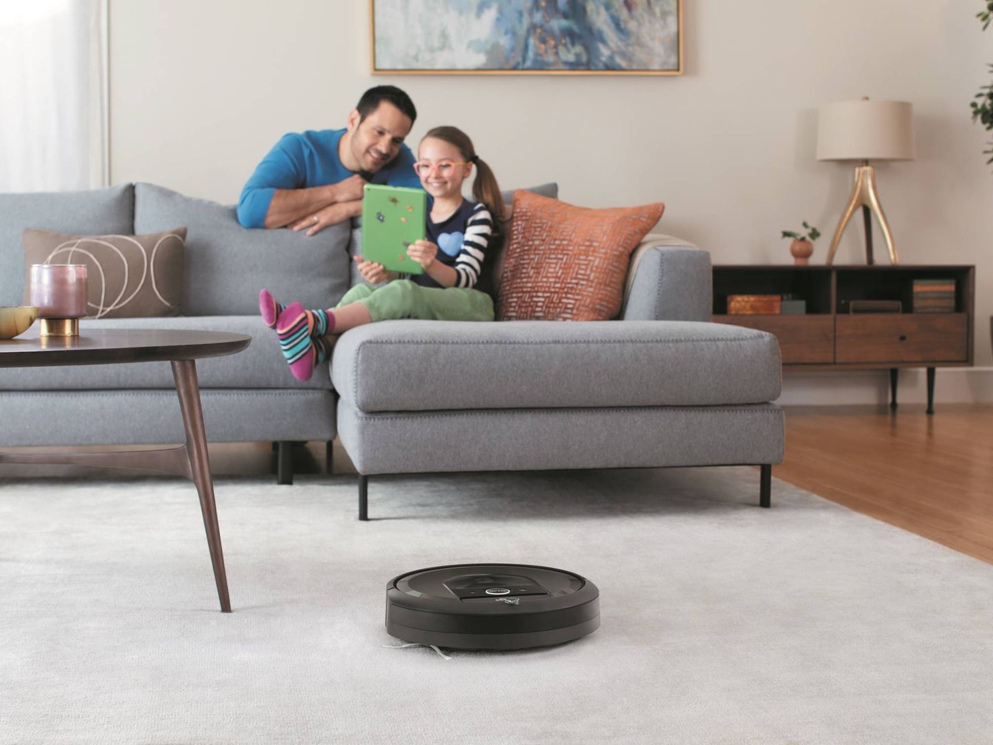 Una pobre Roomba, olvidada en mitad del salón mientras la familia se divierte con una 'tablet' de 2014.