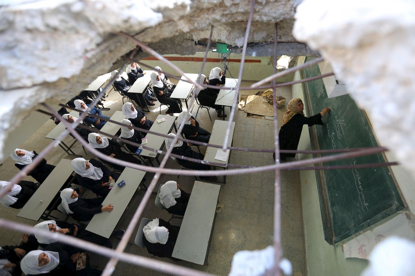 Foto: Estudiantes palestinas fotografiadas desde un boquete en el techo de su escuela, producto de los bombardeos israelíes, en Khan Younis, Gaza, el 24 de agosto de 2015 (Reuters).