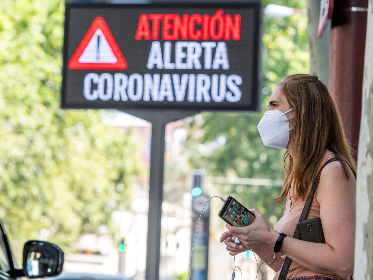 Foto: Una mujer espera el autobús junto a un panel informativo en Sevilla. (EFE)