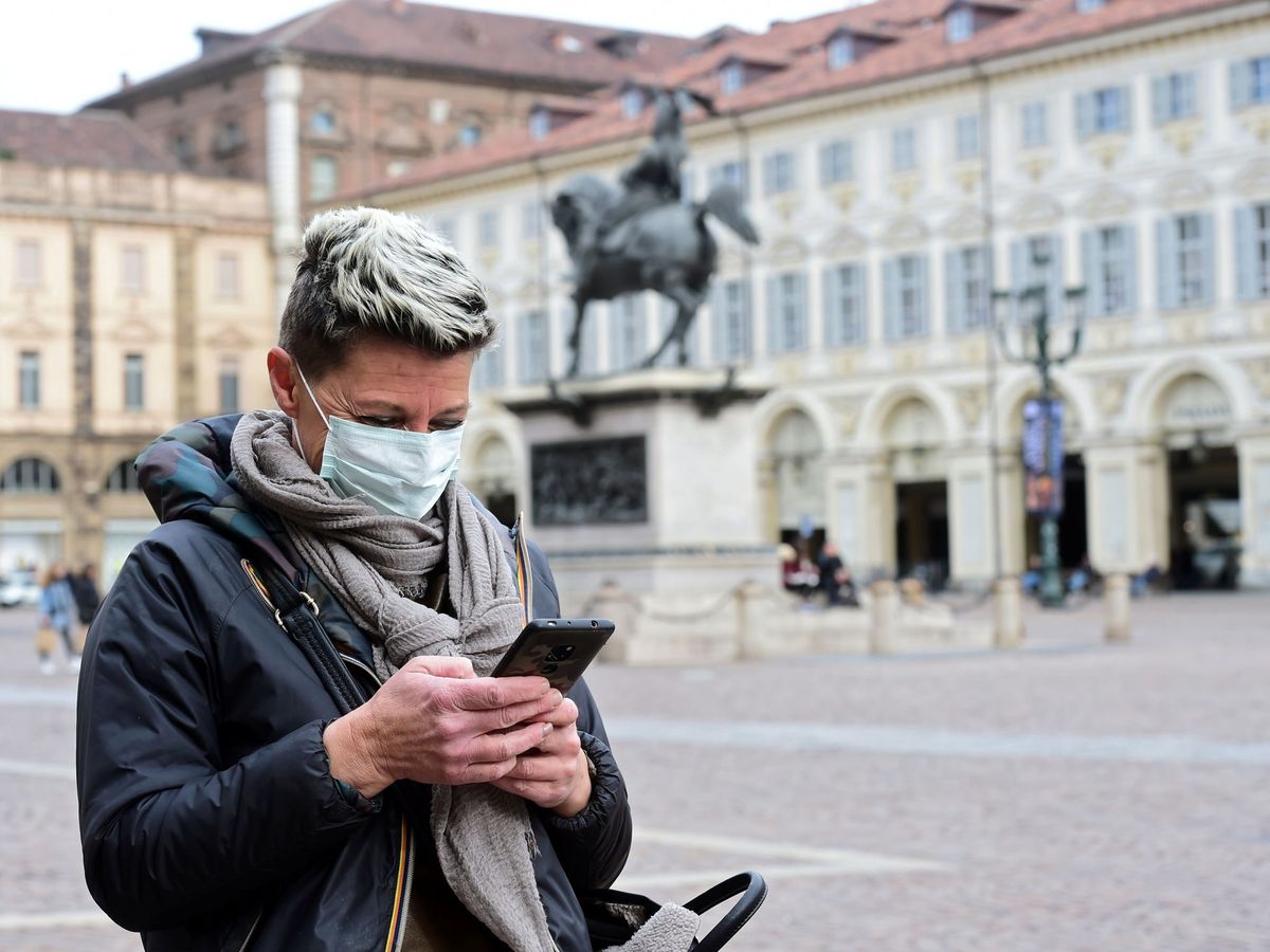 Foto: Una mujer con mascarilla protectora mira su móvil en una plaza de Turín, Italia (REUTERS)