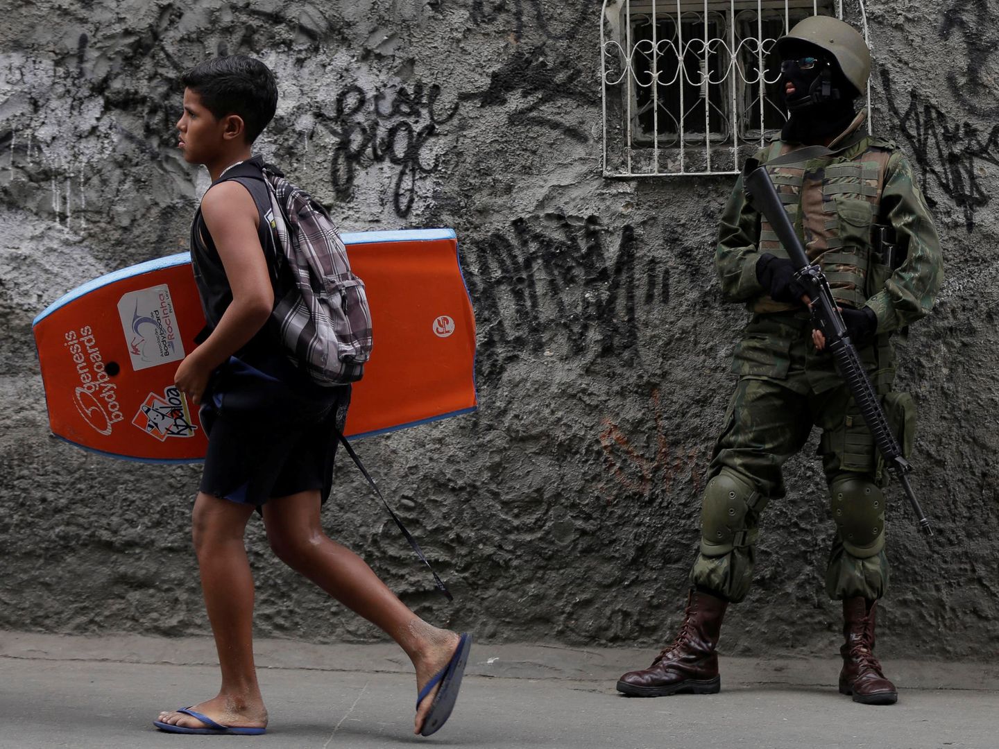 Un joven con una tabla de body-board pasa delante de un soldado desplegado en la favela de Rocinha durante una operación antidroga, en septiembre de 2017. (Reuters)