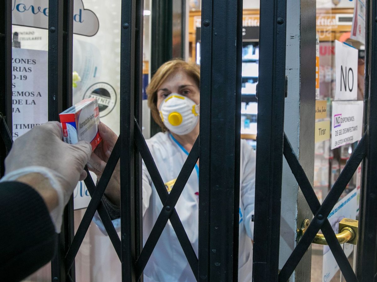 Foto: Una farmacéutica atiende a un cliente a través de la reja de su establecimiento en Zaragoza. (EFE)