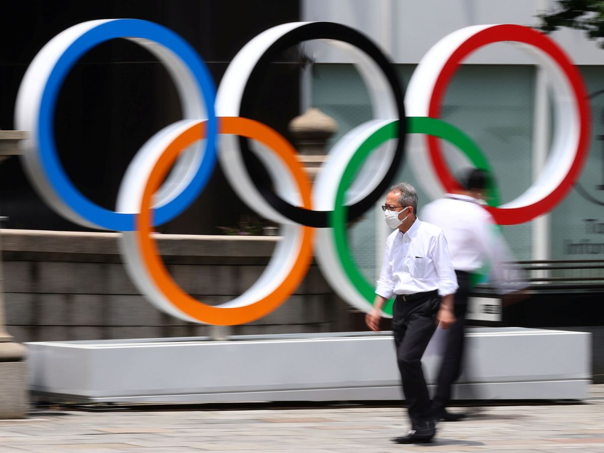 Foto: Un hombre con mascarilla pasa por delante de los anillos olímpicos de Tokio. (Reuters)