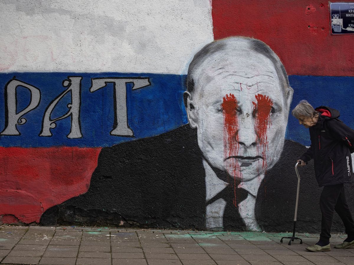 Foto: Una persona camina junto a un mural del presidente ruso Vladimir Putin, que ha sido vandalizado con spray rojo. (Reuters/Marko Djurica)