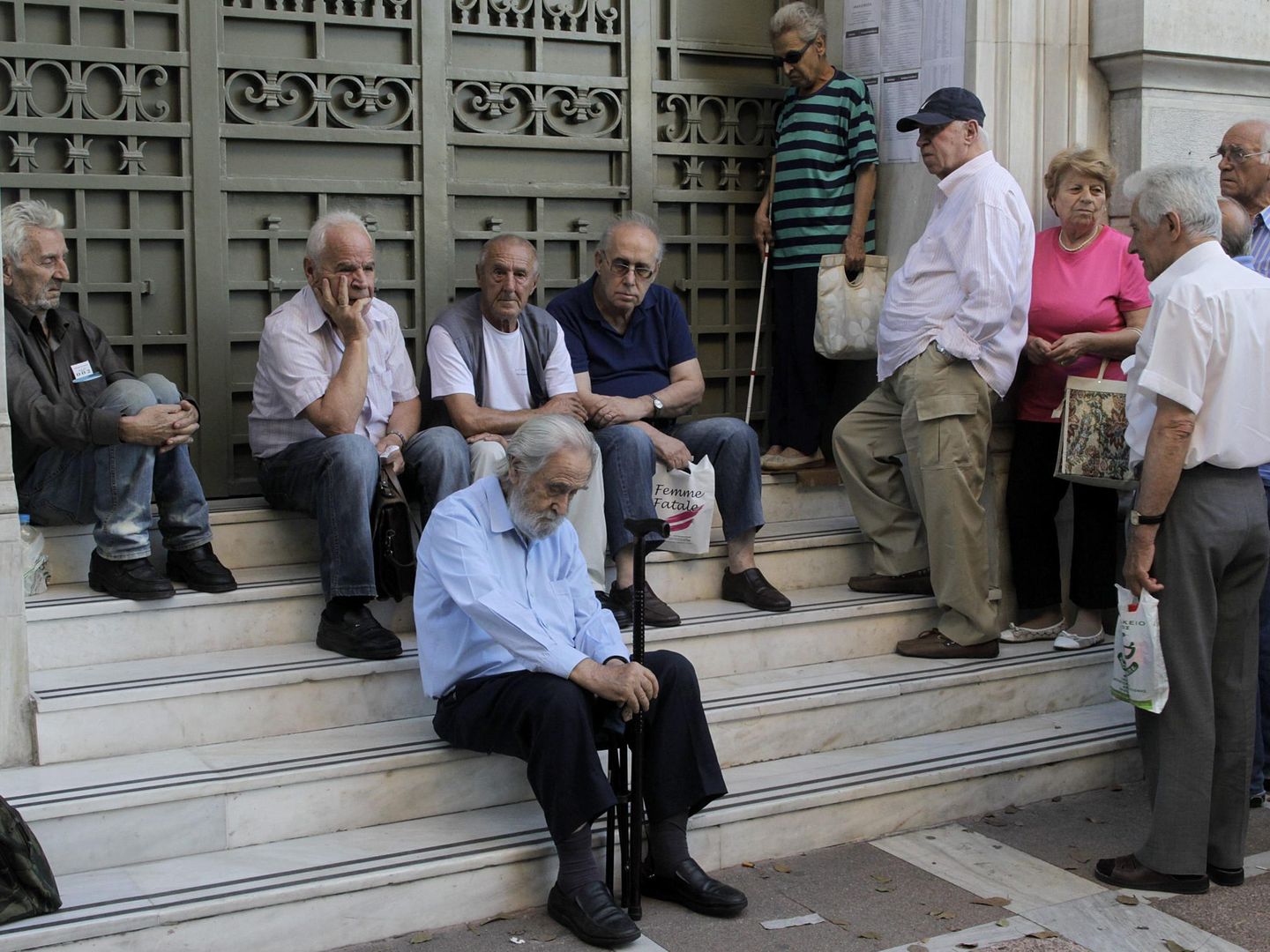 Pensionistas griegos sentados a las puertas de un banco. (Efe)