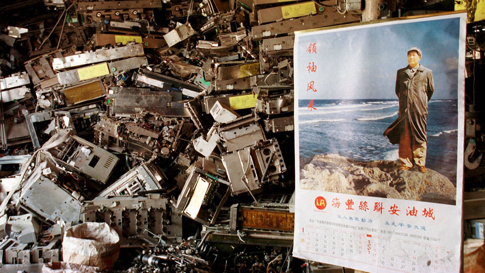 Foto: Basura tecnológica apilada tras un poster de Mao Zedong en la aldea de Yaocuowei, en el sur de China, en 2002. (Reuters)