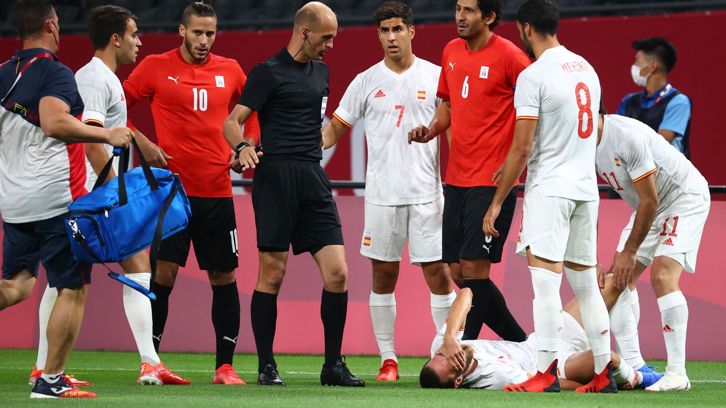 Tokyo 2020 Olympics - Soccer Football - Men - Group C - Egypt v Spain - Sapporo Dome, Sapporo, Japan - July 22, 2021. Oscar Mingueza of Spain reacts after sustaining an injury as Ahmed Hegazy of Egypt reacts alongside referee Adham Makhadmeh REUTERS Kim Hong-Ji