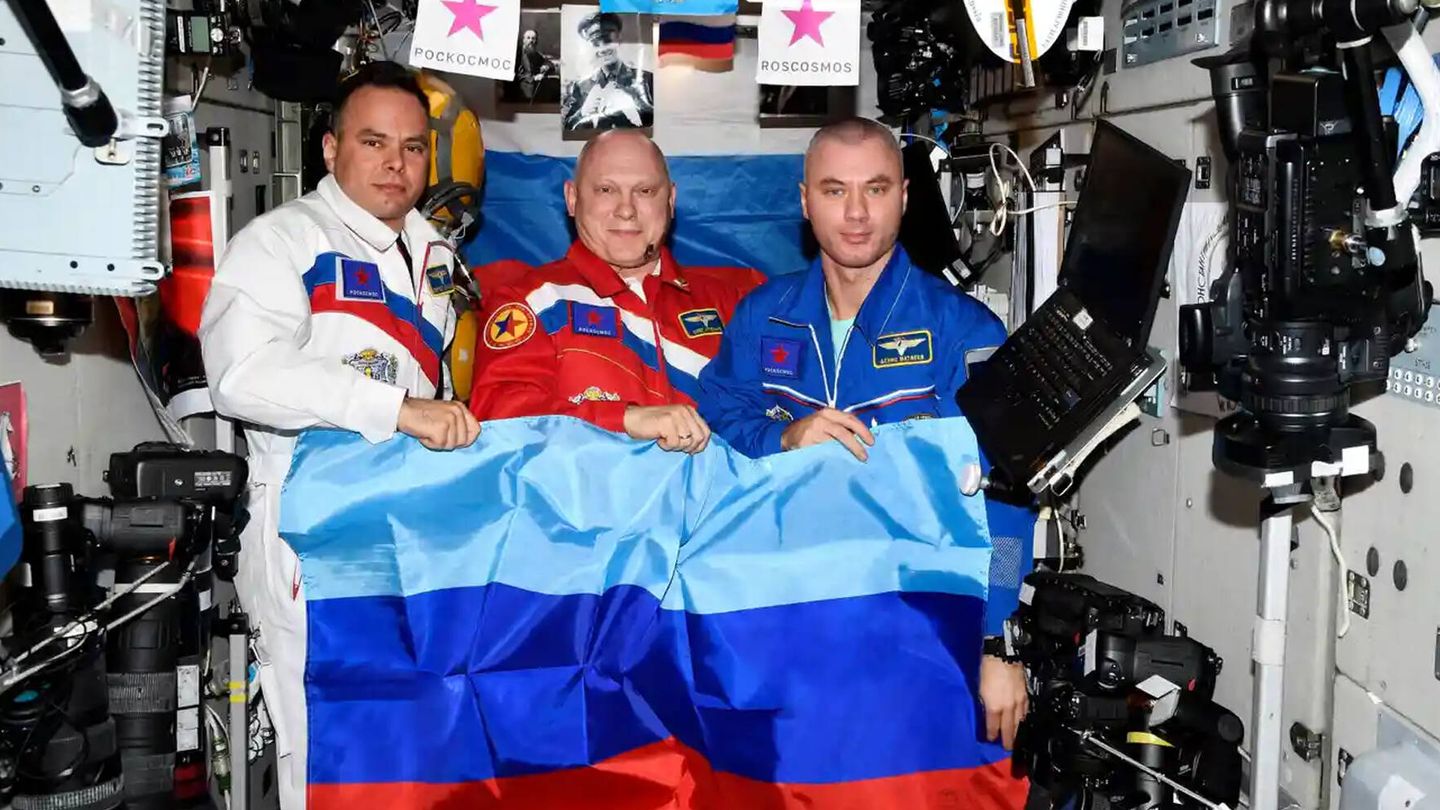 Los cosmonautas rusos Oleg Artemyev, Denis Matveev y Sergey Korsakov con la bandera de la república no reconocida de Luhansk. (Roscosmos)