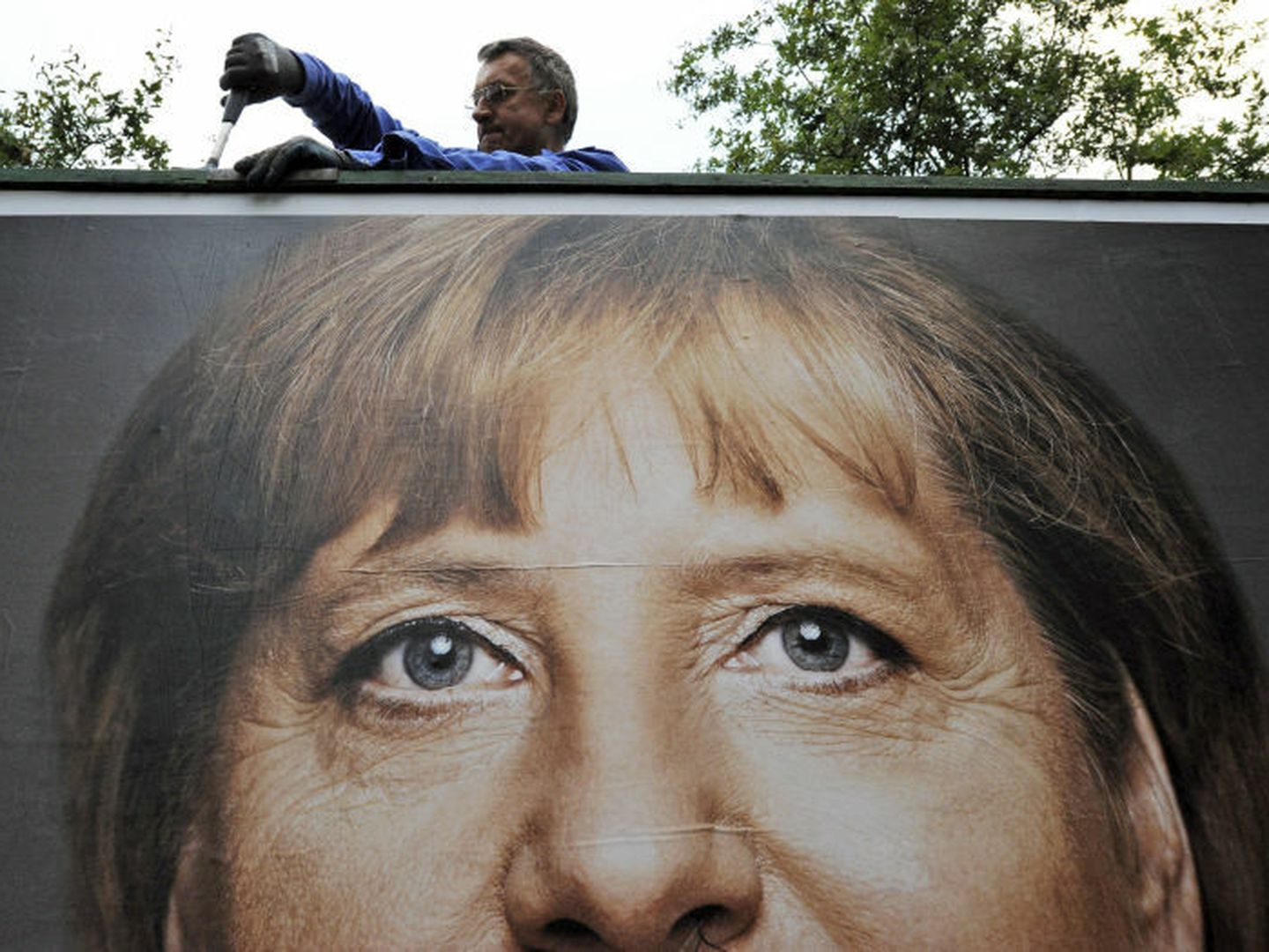 Un trabajador retira un cartel electoral con el rostro de la canciller en Itzehoe, Alemania (Efe).