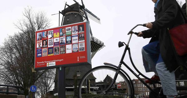 Foto: Una mujer ciclista pasa por delante de un cartel electoral y un molino en Ámsterdam, el 14 de marzo de 2017. (Reuters)