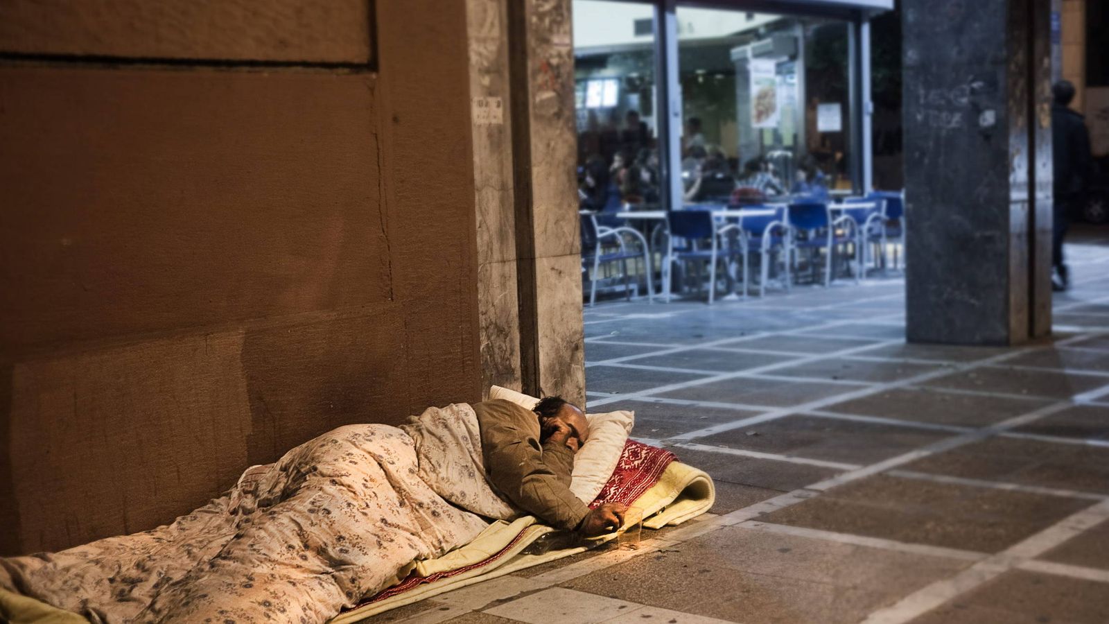 Foto: Un hombre 'sin techo' duerme en la acera, junto a una cafetería. (EFE)
