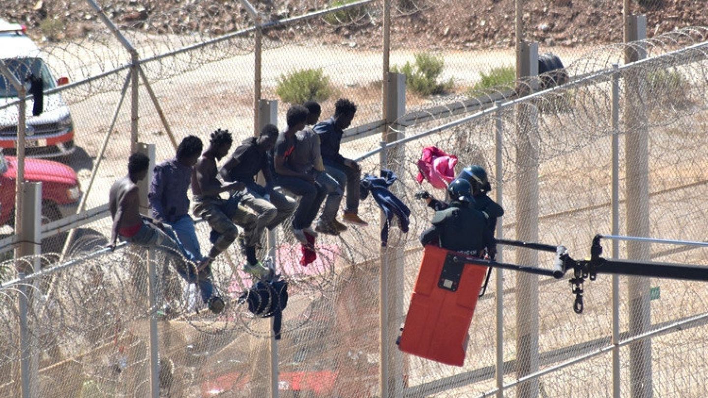 Dos agentes descuelgan de la valla a varios migrantes encaramados durante un salto. (EFE)