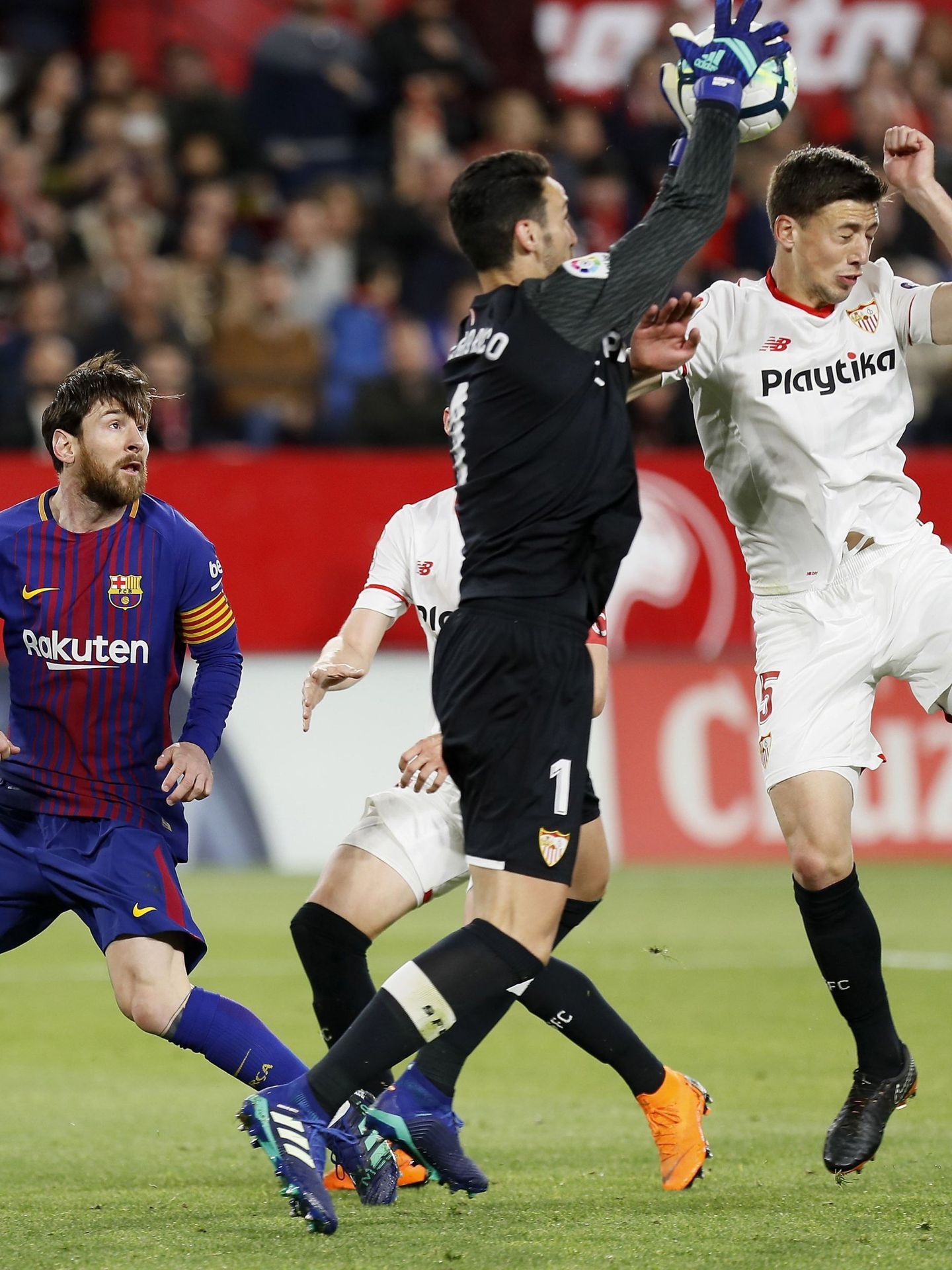 Sergio Rico sale por arriba a blocar un balón ante la mirada de Messi. (EFE).