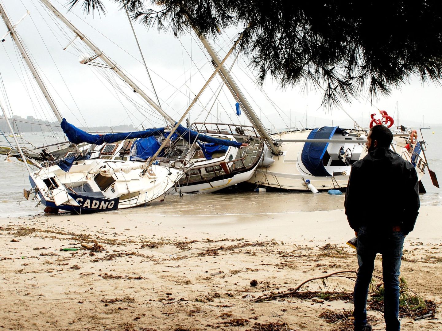Un hombre mira tres de las embarcaciones varadas en la arena en el Port de Pollença (Mallorca) (EFE)