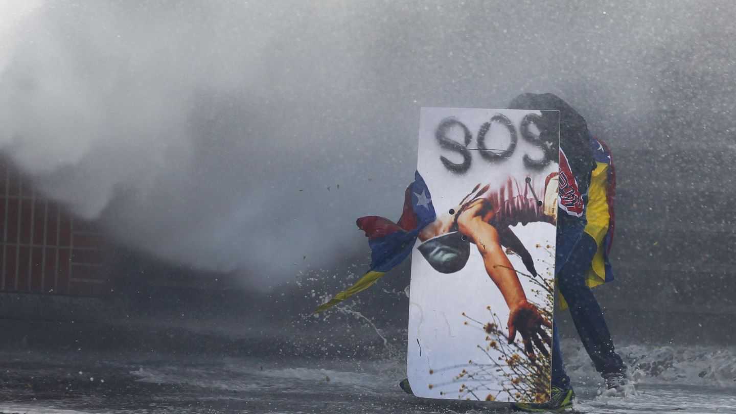 Un manifestante opositor se protege de un cañón de agua de la Policía en Caracas (Reuters).