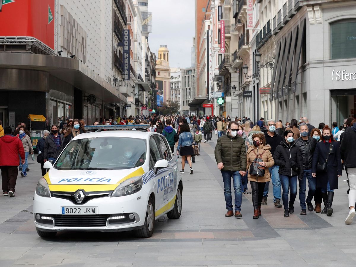 Foto: Un coche de la policía local circula entre los transeúntes que pasean por una de las calles comerciales anexas a la Puerta del Sol en Madrid. (EFE)