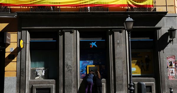 Foto: Un cajero de CaixaBank bajo una bandera española en Madrid. (Reuters)