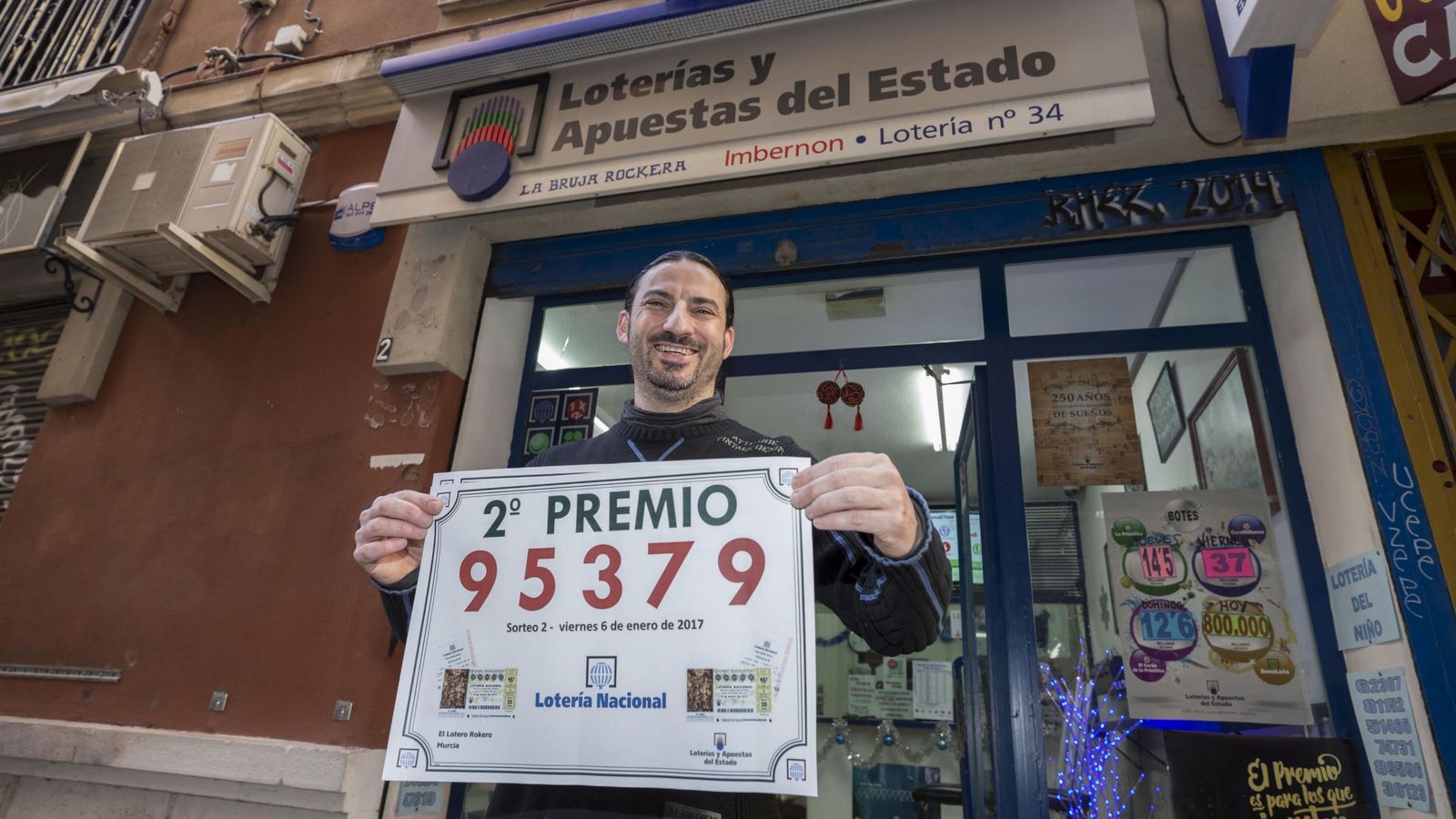 Foto: El gerente de la administración de loterias La Bruja Rockera, la número 34 de Murcia, José María Imbernon, muestra el cartel del segundo premio del sorteo del Niño. (Efe) 