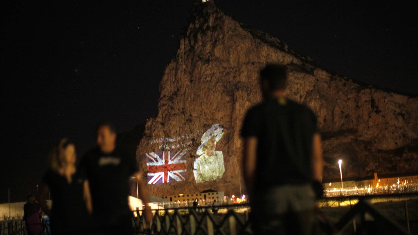 Varias personas observan una imagen de Isabel II y la bandera británica en el Peñón. (Reuters)