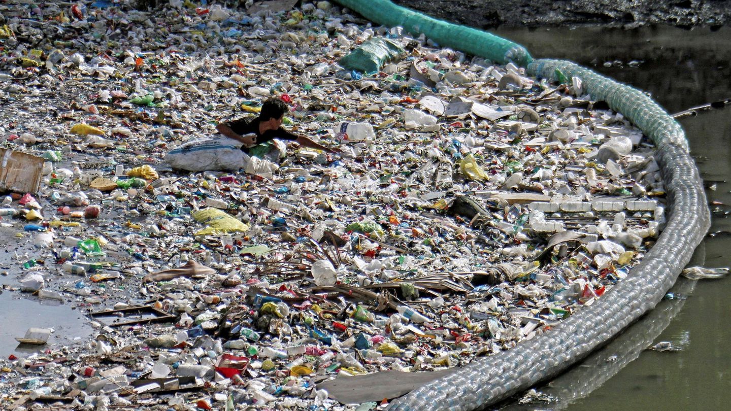 Un hombre recolecta botellas de plástico entre los residuos que una malla impide que alcancen el mar en un río en Cebu (Filipinas) el 7 de junio de 2019. (EFE)