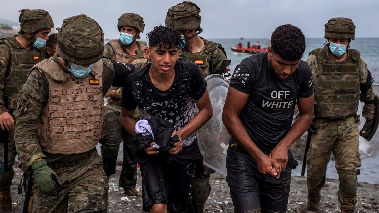 Soldados del Ejército ayuda a dos migrantes a salir del agua en la playa de El Tarajal. (EFE)