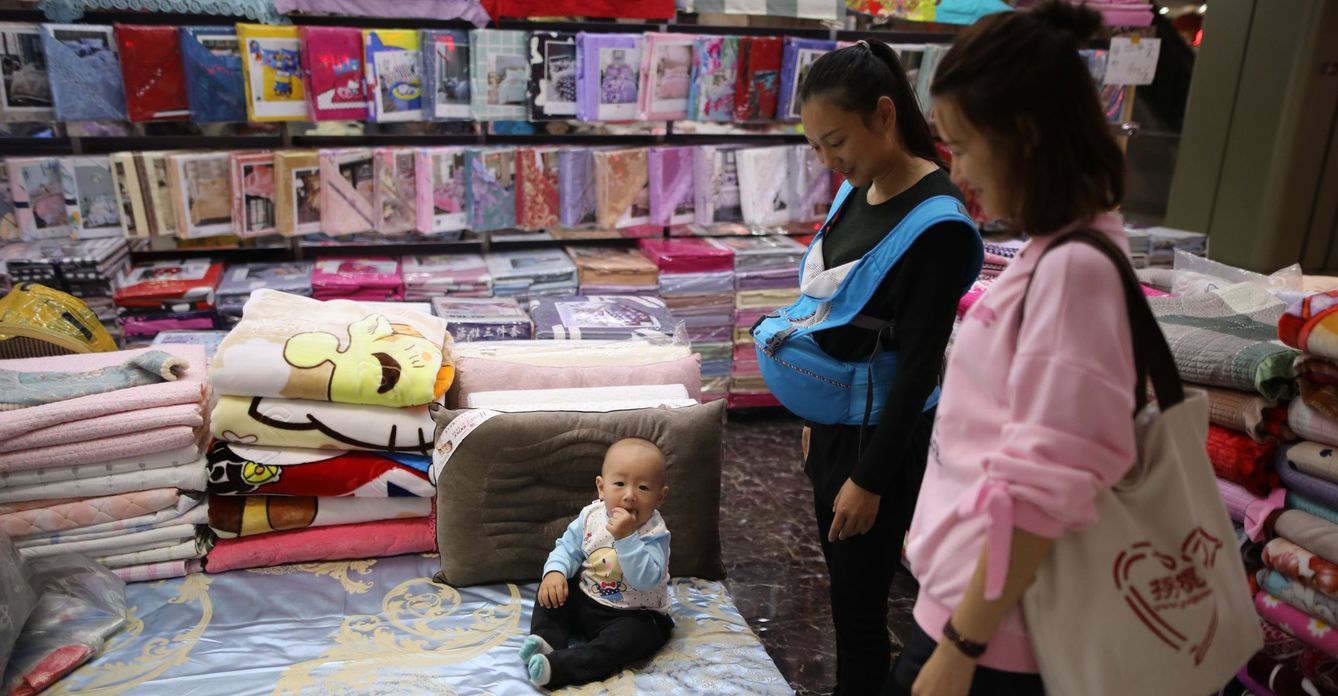 Dos clientas miran a un bebé que juega en un puesto de un mercado de mayoristas en Pekín (China). (EFE)