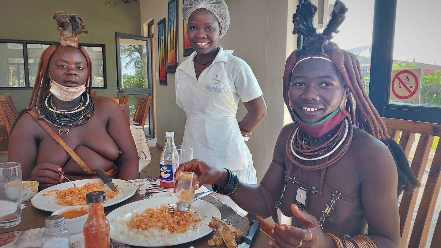 Mukahoveka y Pokajuru de izquierda a derecha, comiendo arroz y carne en un restaurante junto a Ndunge, una himba moderna. (J. Brandoli)