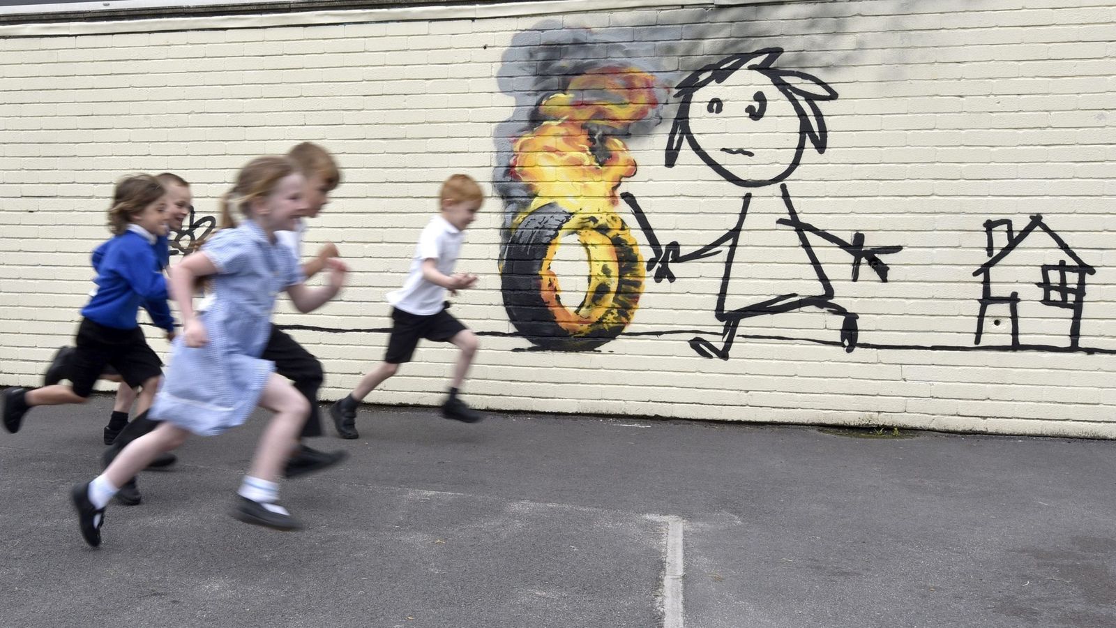 Foto:  Niños corren por el patio de su colegio, el Bridge Farm Primary School, junto a un mural de Banksy. (EFE)