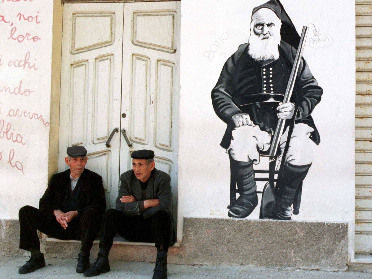 Foto: Dos ancianos sentados frente a una casa de Orgosolo, un pueblo de Cerdeña en el que los murales son la principal forma de expresión artística.