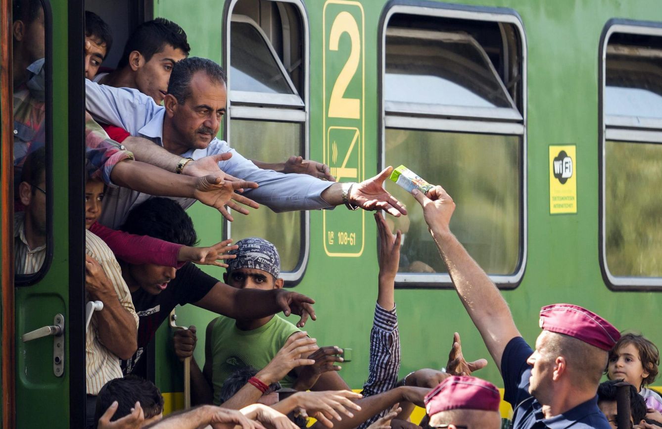 Un policía entrega zumo y frutas a los refugiados en la estación ferroviaria de Bicske (Hungría). (EFE)