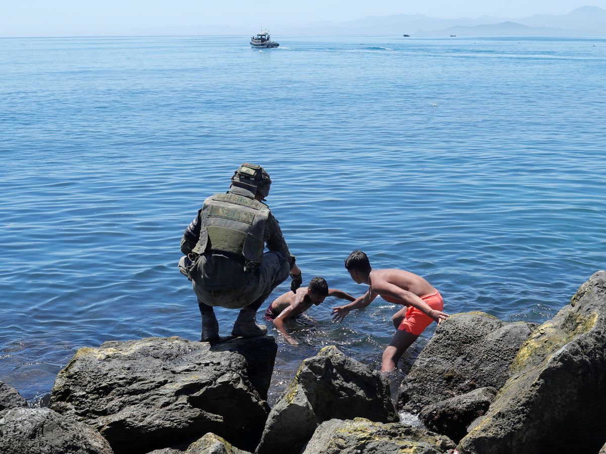Foto: Un miembro del Ejército auxilia a dos niños que han cruzado a nado la frontera entre Marruecos y Ceuta. (Reuters)