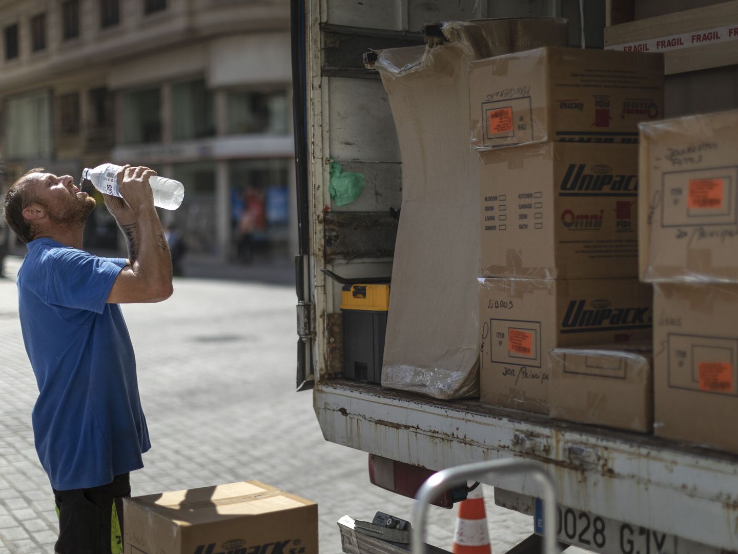 Un trabajador de una empresa de mudanzas bebe agua para combatir el calor en una calle del centro de Valencia. (EFE/Biel Aliño).