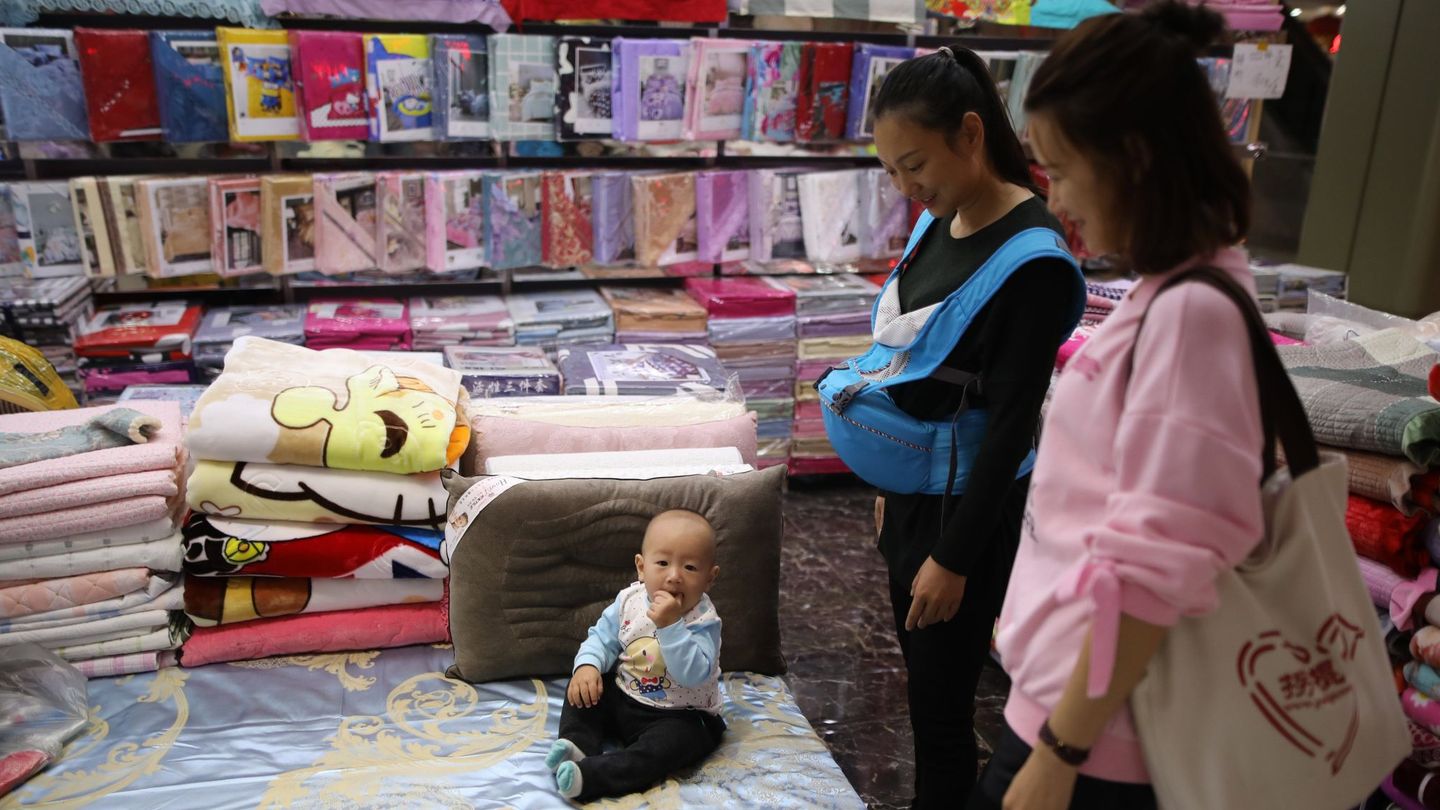 Dos clientas miran a un bebé que juega en un puesto de un mercado de mayoristas en Pekín (China). (EFE)