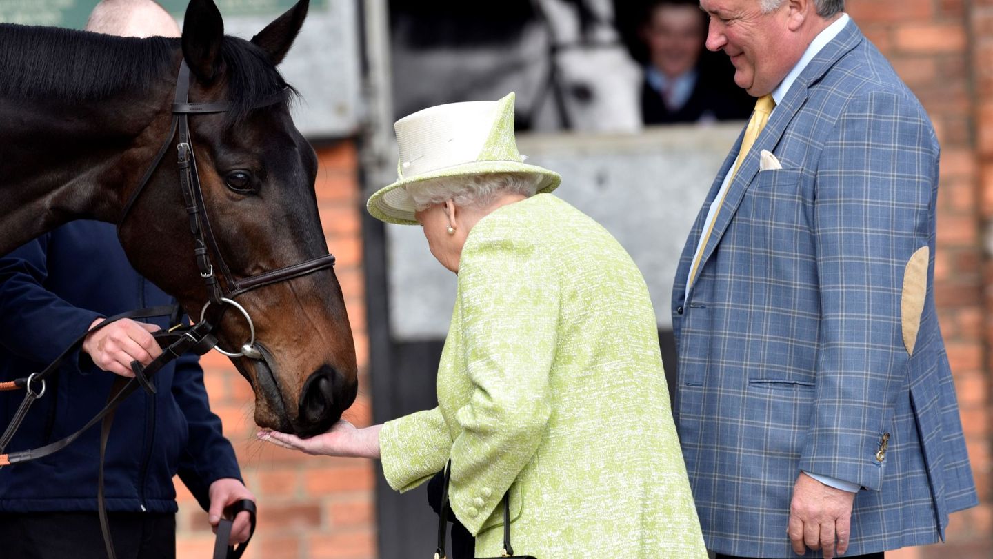 La reina Isabel II acaricia un caballo junto al entrenador ecuestre del equipo británico de caza, Paul Nicholls, en marzo de 2019.