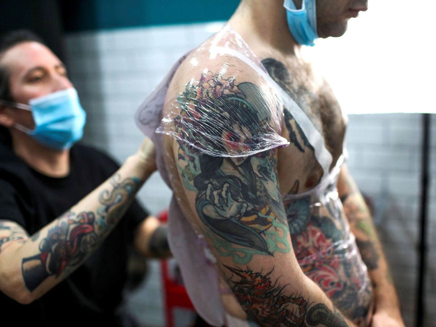 Un tatuador trabajando sobre la espalda de un joven. Foto: EFE David Fernández